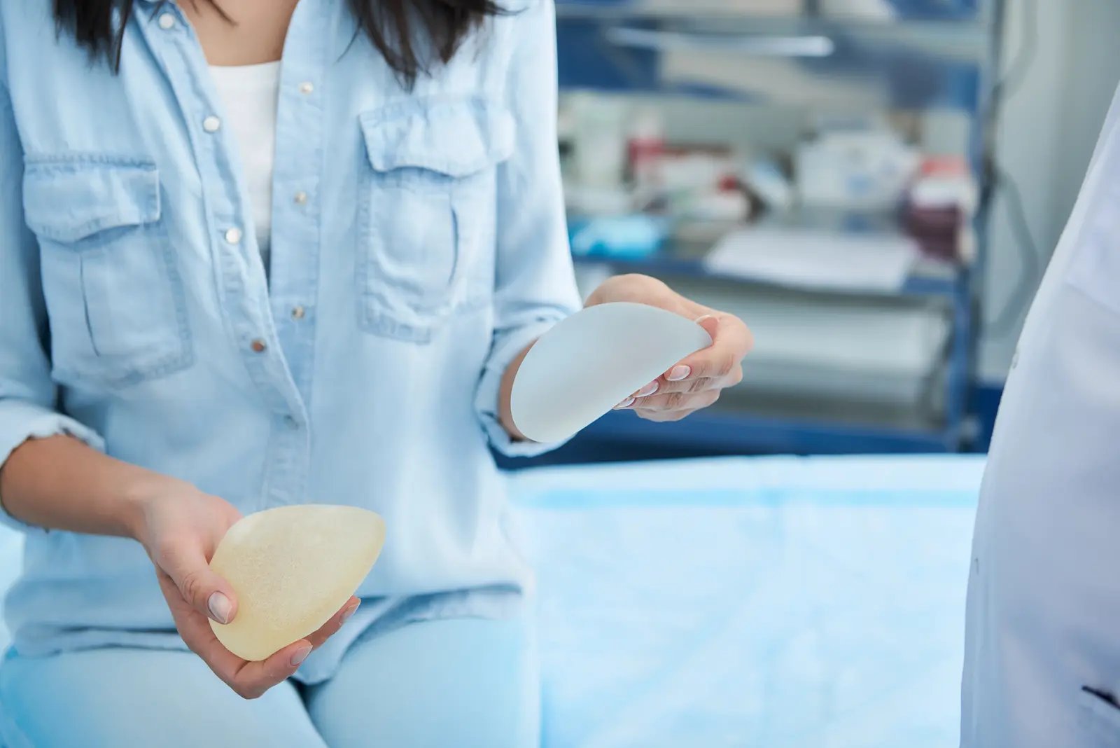 Person holding silicone breast implants in a medical office setting.