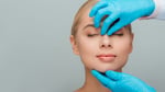 cropped view of beautician in latex gloves touching nose of naked woman isolated on grey