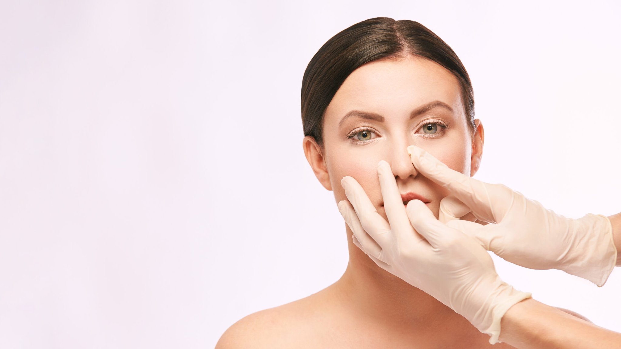 Plastic surgeon using gloved hands to examine a patient's nasal structure for reconstructive rhinoplasty and congenital defect correction